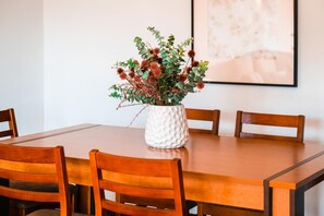 Una mesa de comedor con un florero blanco texturizado que contiene follaje verde y flores rojas.