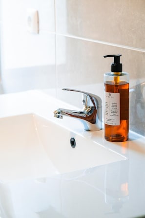 A bathroom sink with a chrome faucet and a bottle of liquid soap.