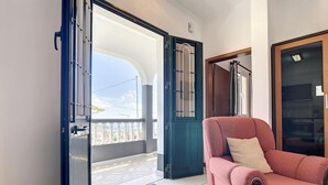 Una habitación con un sillón rojo, una puerta que da a un balcón y vista al cielo.