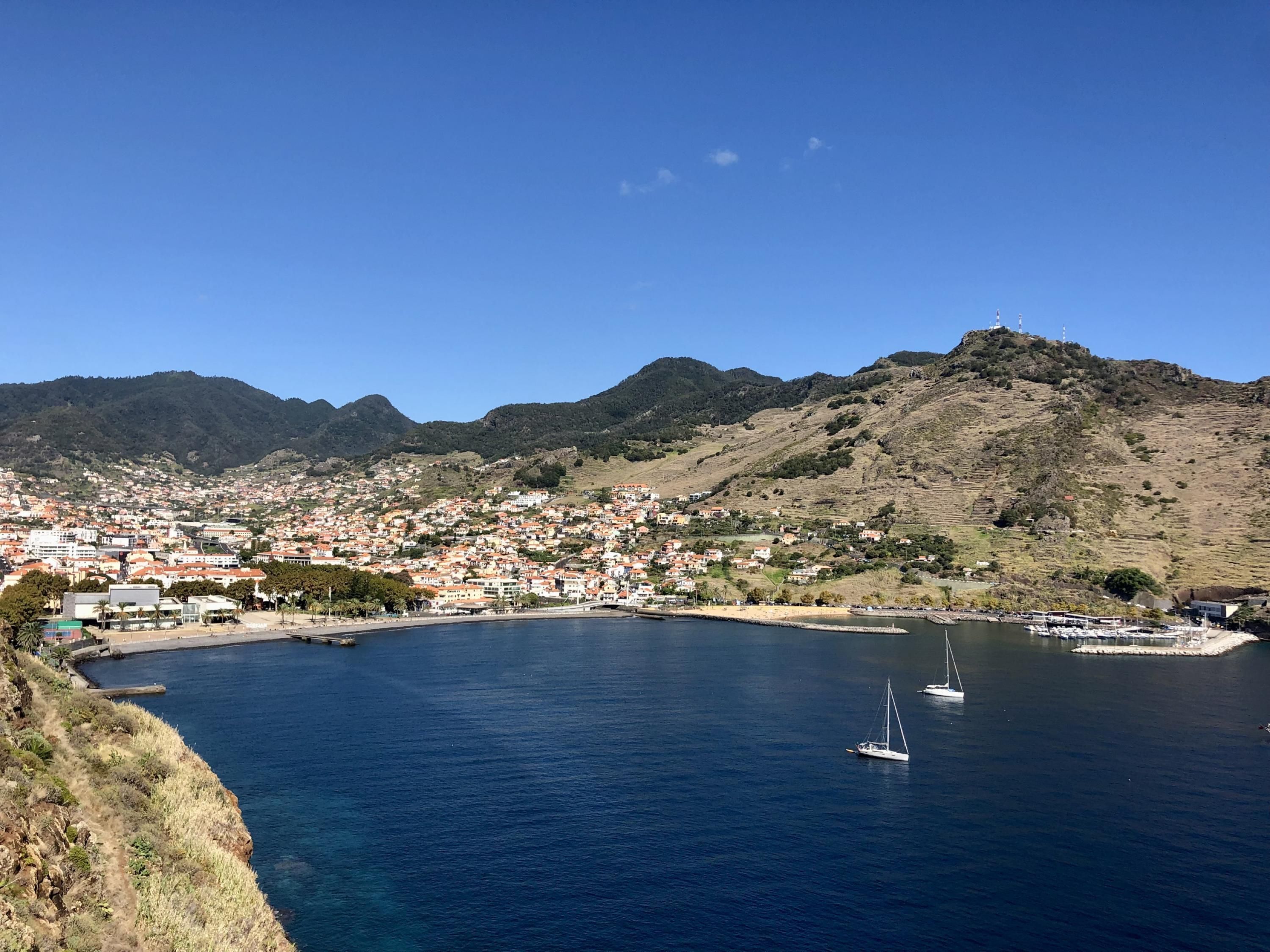 A coastal town with a marina, boats, and a mountainous backdrop.