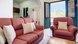 Sala de estar con sofá rojo y sillón, una mesa de centro de madera, y vista a la montaña desde una puerta.