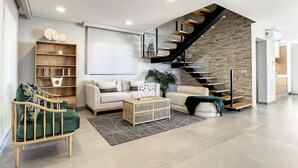 Un salon moderne comprenant un canapé, une table basse, une bibliothèque, un escalier et un écran de projection fixé au mur.