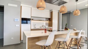 Une cuisine moderne avec des meubles blancs, un îlot central et trois suspensions en osier.