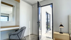 Une chambre moderne avec un fauteuil gris, une table de chevet avec une lampe et une porte-fenêtre coulissante donnant sur un balcon.