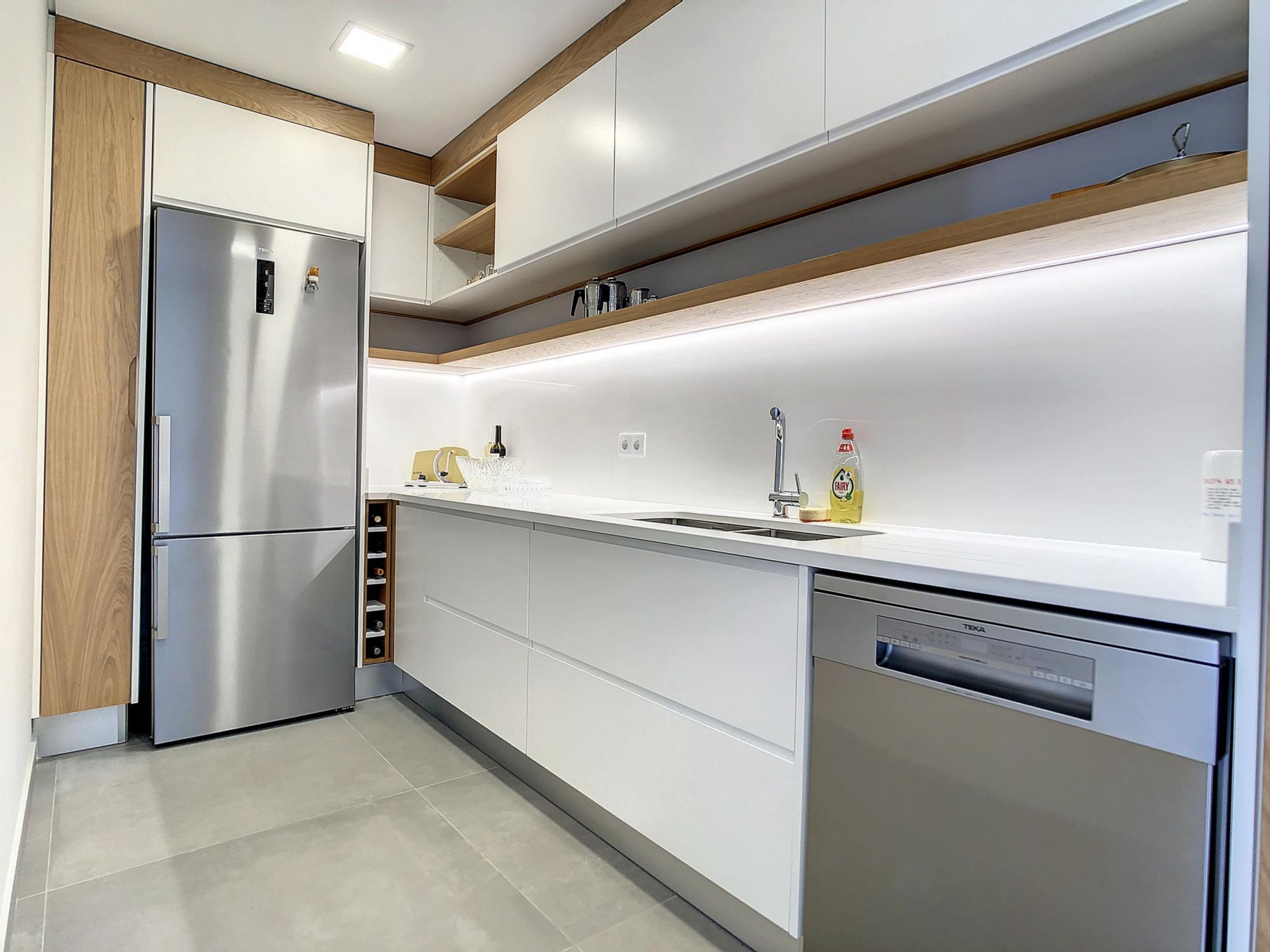 A modern kitchen with a stainless steel refrigerator, a dishwasher, and a white countertop.