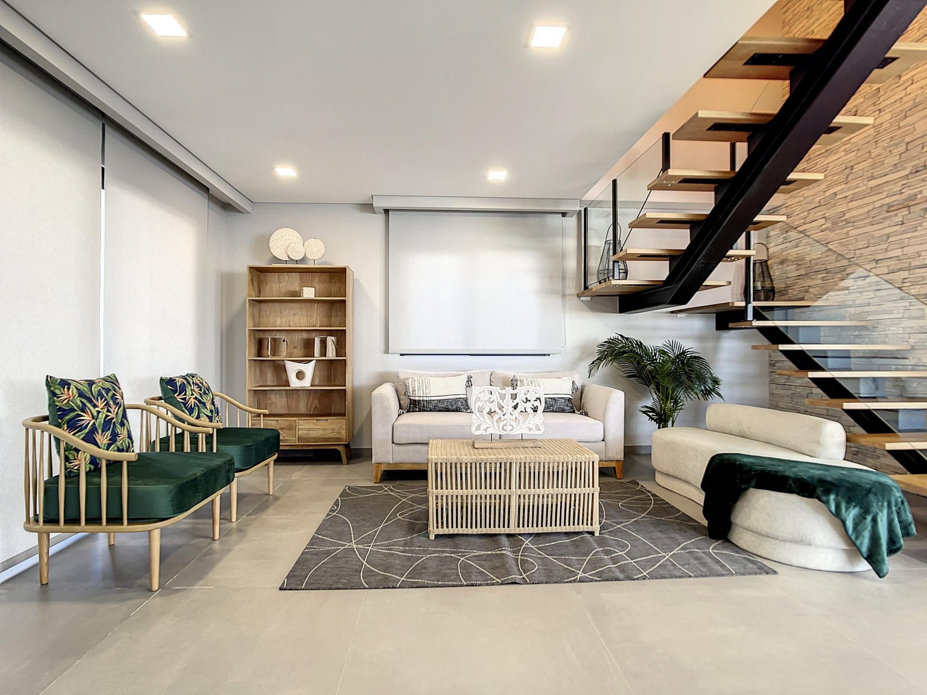 A modern living room with a sofa, chairs, a coffee table, a bookshelf, and a staircase.