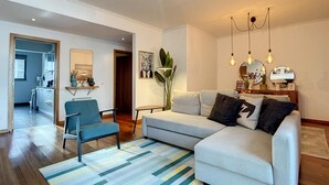 A modern living room with a sofa, armchairs, a coffee table, and a striped rug. There is a kitchen area in the background with a dining table and chairs. - Terrace Apartment by Atlantic Holiday (Funchal)