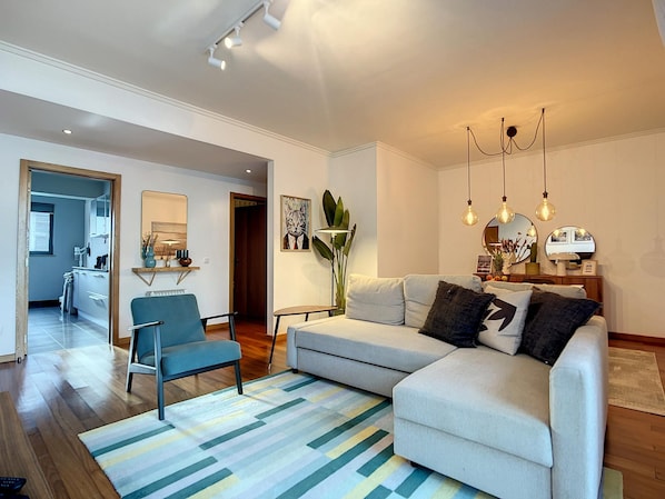 A modern living room with a sofa, armchairs, a coffee table, and a striped rug. There is a kitchen area in the background with a dining table and chairs. - Terrace Apartment by Atlantic Holiday (Funchal)