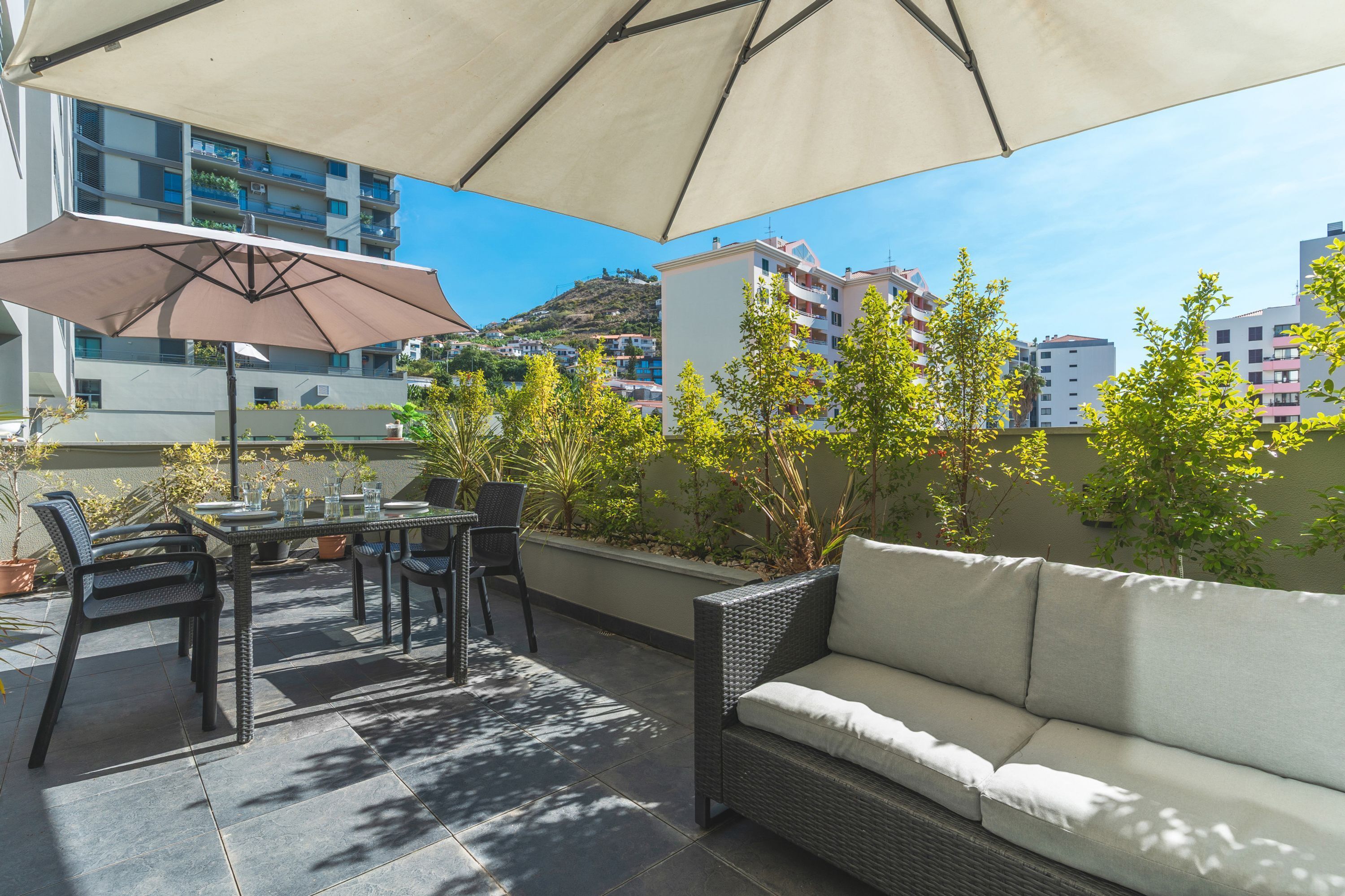 An outdoor patio with a table, chairs, and a sofa under a large umbrella.