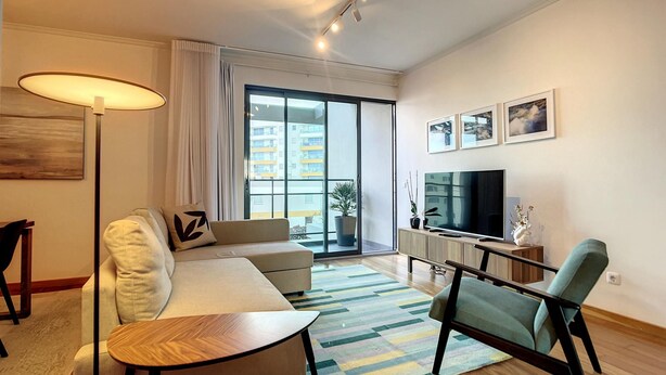 A modern living room with a sofa, a coffee table, a TV, and a large window with a view of buildings. - Terrace Apartment by Atlantic Holiday (Funchal)