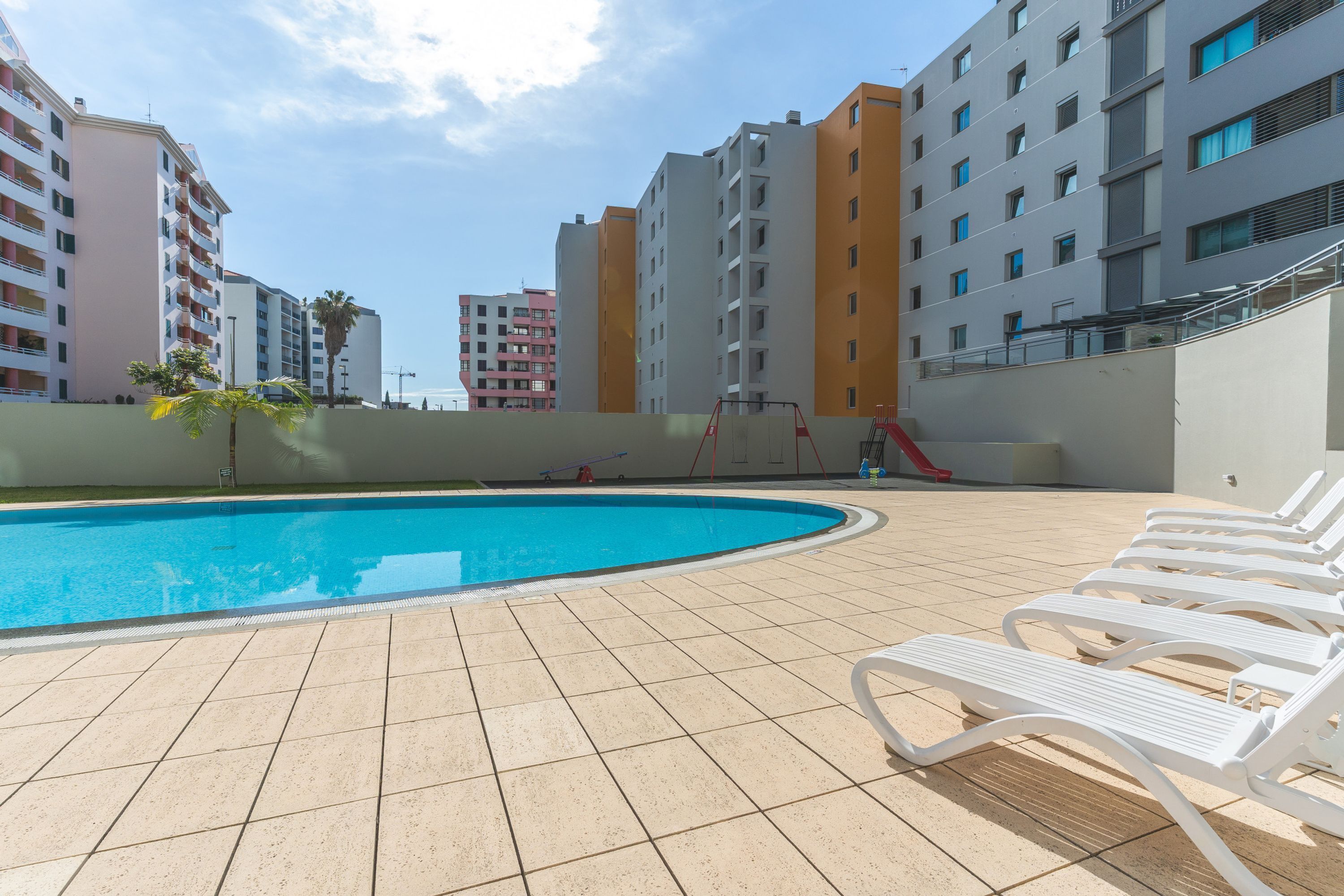 Una piscina con lettini, uno scivolo e moderni edifici sullo sfondo.