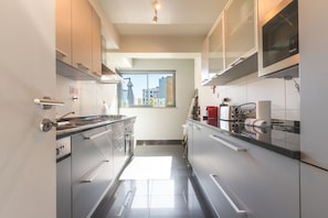 A modern kitchen with stainless steel appliances, a window with a view of buildings, and a tiled floor.