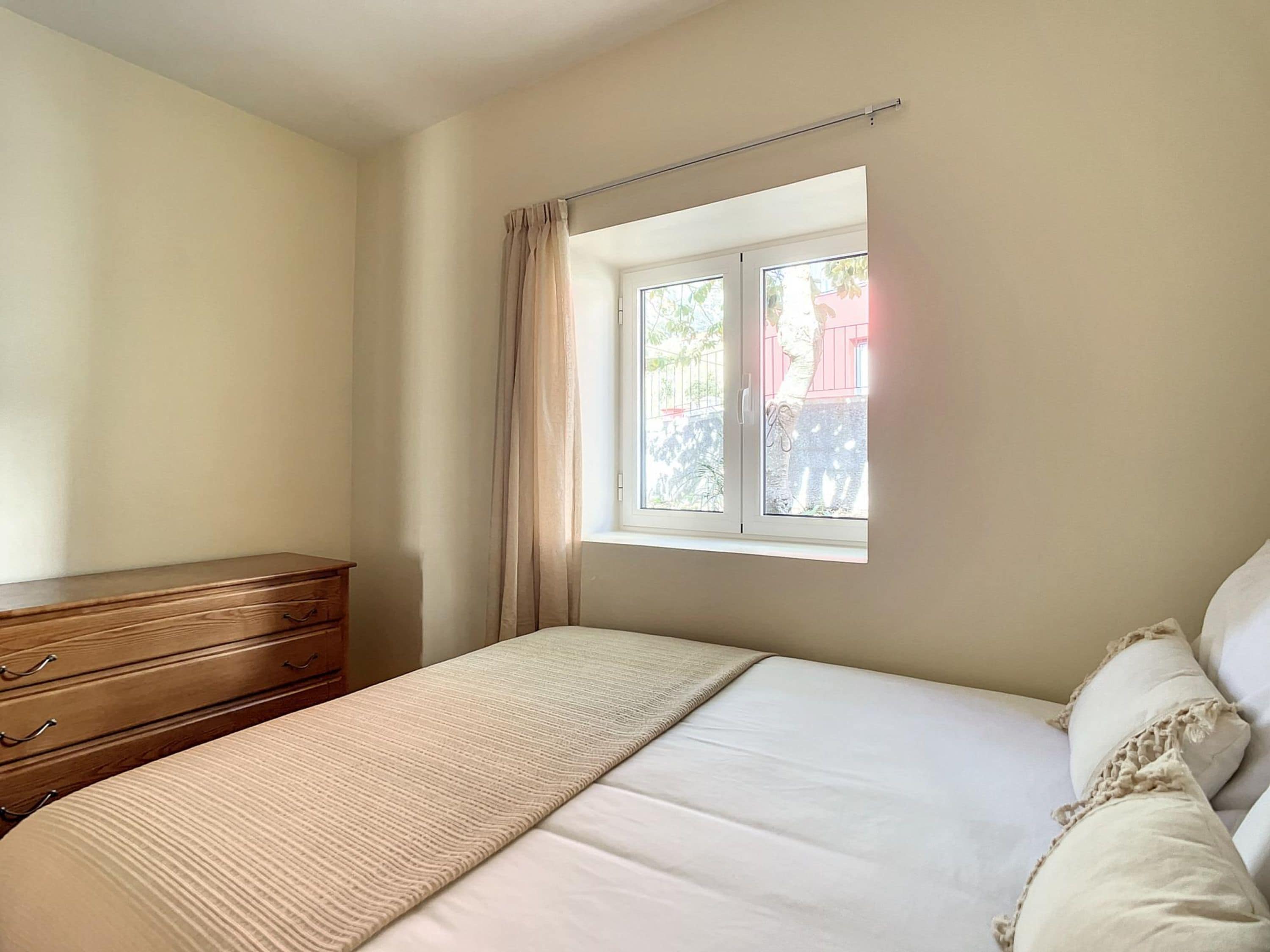 Un dormitorio con una cama, un aparador de madera y una ventana con cortinas.