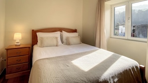 Uma cama bem arrumada com cabeceira de madeira, luminária de cabeceira e janela com cortinas.