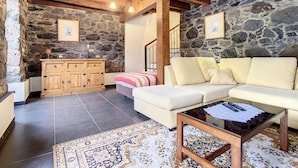 Uma sala de estar acolhedora com parede de pedra, vigas de madeira, sofá, mesa de centro e um armário.