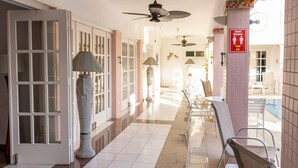 Un passadís d'hotel amb sòl de rajola, ventilador al sostre, un gran vas i un senyal de distància social.