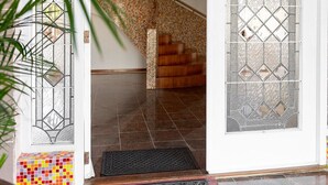 Una escala amb una paret de mosaic, una porta amb un panell de vidre decoratiu i un felpó de benvinguda.