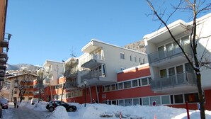 A residential area with multi-story buildings, some with balconies, and a road partially covered with snow.