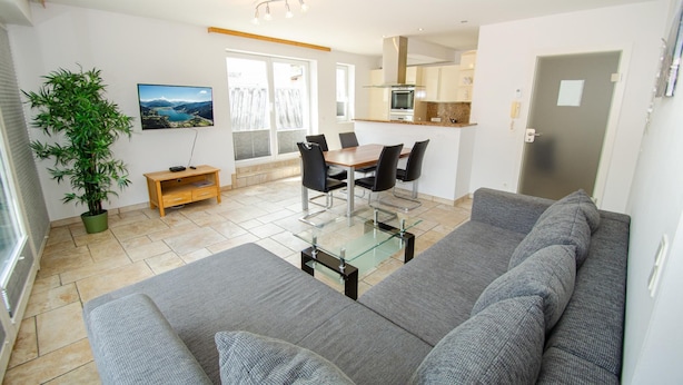 A modern living room with a grey sofa, a glass coffee table, and a dining area with a wooden table and chairs.