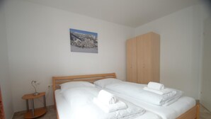 A bedroom with two beds, a wooden wardrobe, a small table, and a picture on the wall.