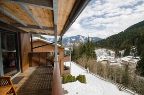 Un balcon en bois offrant une vue sur des montagnes enneigées et un village.