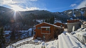 Een houten hut met balkon, omringd door besneeuwde bergen en een heldere lucht.