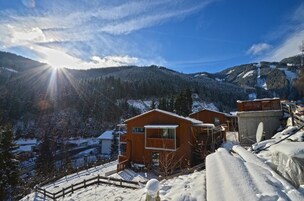 Una cabaña de madera con balcón, rodeada de montañas nevadas y un cielo despejado.
