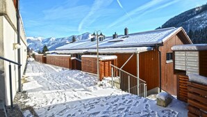Een besneeuwde buitenplaats met houten hutten en een berg op de achtergrond.