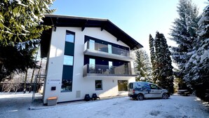 A modern two-story building with balconies, a sign indicating it is an apartment house, and a parked van with a logo. - 5 Seasons House Zell am See - TOP 1 Summer Card (Zell am See)