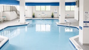 Una piscina interior con agua cristalina, rodeada de paredes blancas y detalles azules, con una escalera y una zona de estar a la vista.
