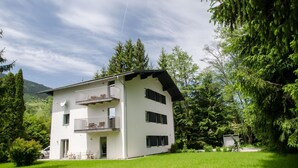 A two-story white building with a balcony on the upper floor, surrounded by lush greenery and trees. - 5 Seasons House Zell am See - TOP 4 Summer Card (Zell am See)