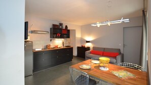 A compact kitchen with modern appliances, a dining area with a wooden table and metal chairs, and a grey sofa with red cushions. - 5 Seasons House Zell am See - TOP 4 Summer Card (Zell am See)