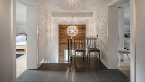 Un couloir au design moderne, agrémenté d’un mur d’accent en bois, d’un luminaire décoratif et de deux chaises.