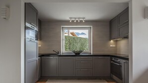 Une cuisine moderne avec des armoires grises, un four encastré, une fenêtre donnant sur un espace verdoyant et un luminaire placé au-dessus de la fenêtre.