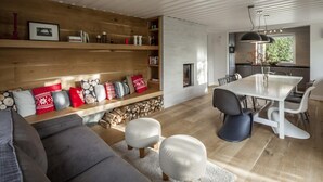 Un salon moderne avec un canapé gris, des poufs blancs, une bibliothèque en bois et un coin repas comprenant une table et des chaises blanches.