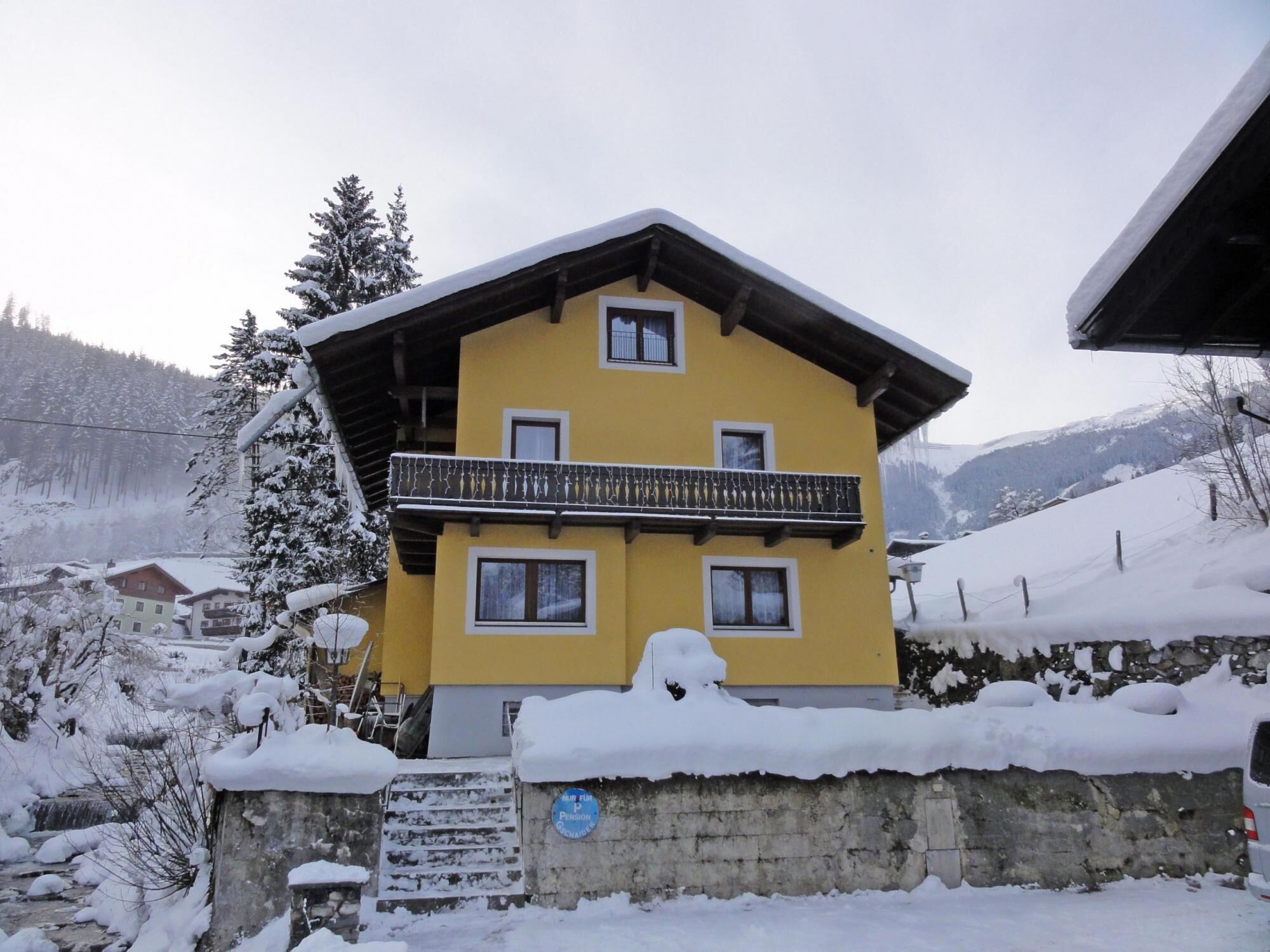 A yellow building with a balcony, surrounded by snow-covered trees and mountains.