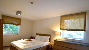 Un dormitorio con cama, mesitas de noche, cómoda y dos ventanas con cortinas.