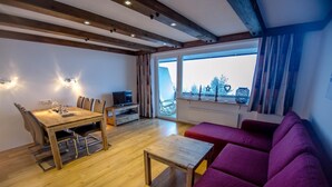 Una sala de estar moderna con una mesa de comedor de madera, un sofá morado y un televisor sobre un mueble.