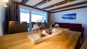 Una mesa de comedor de madera con un centro de mesa de cristal, un sofá rojo y vistas al exterior a través de un amplio ventanal.