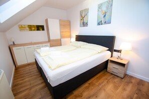 A modern bedroom with a large bed, a bedside table, a nightstand, a wardrobe, and artwork on the walls.