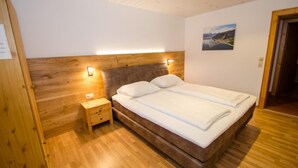 A bedroom with a wooden headboard, two beds, a nightstand, and a wall-mounted lamp.