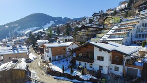 A snow-covered residential area with houses, a winding road, and mountains in the background.