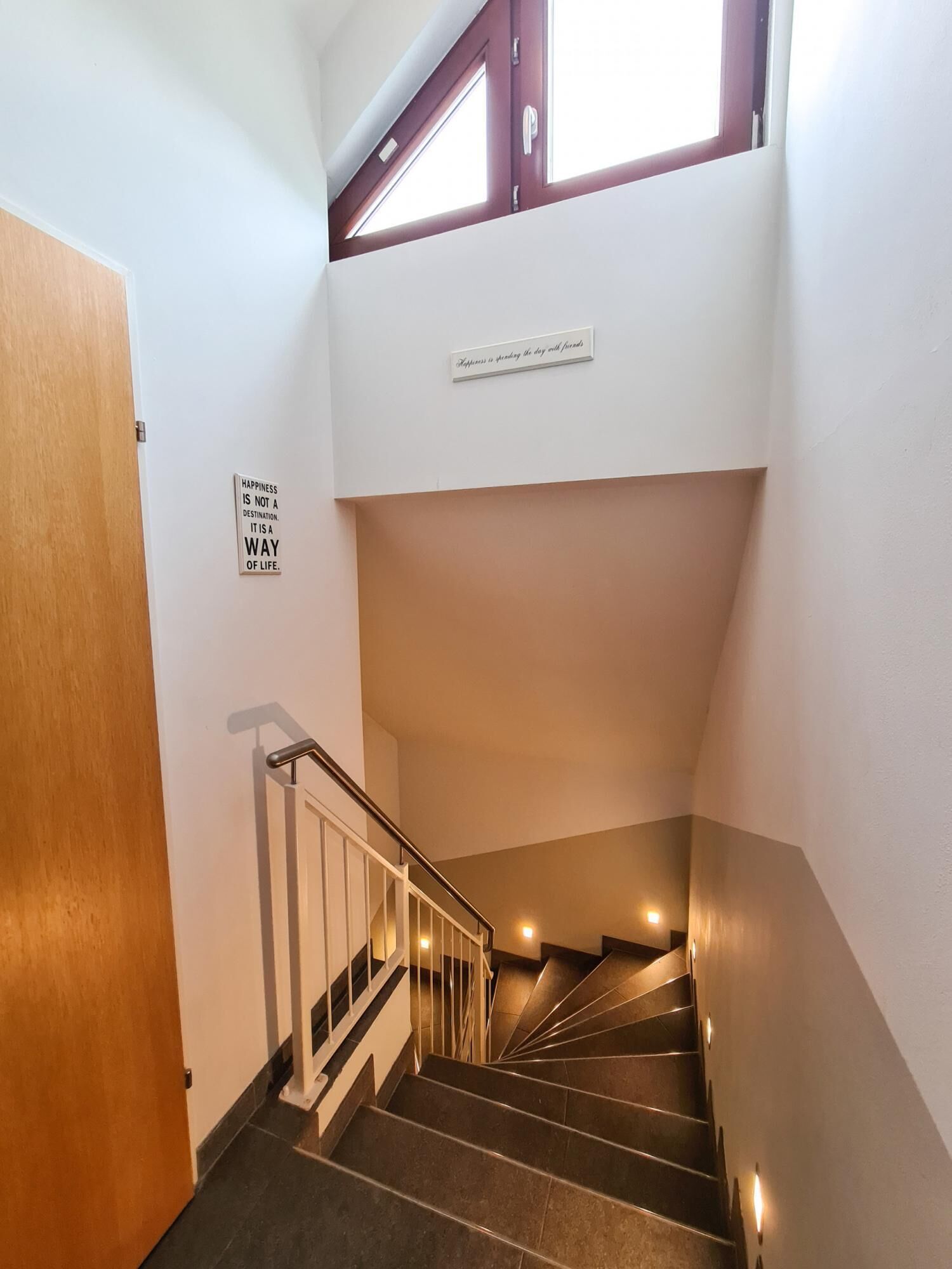 Eine Treppe mit Handlauf, eine Holztür und zwei Schilder an der Wand.