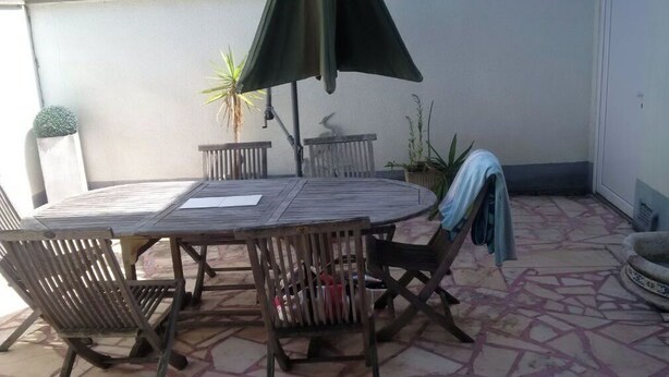 A wooden table with chairs and a green umbrella, surrounded by potted plants on a tiled patio. - House in the center of town, close to the sea (Cabourg)