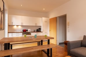 A modern kitchen with white cabinets, a wooden dining table, and a grey sofa.