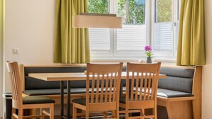 A dining area with a wooden table and chairs, a bench, and a window with green curtains. - Fourteen 2 1 Zell am See S P (Zell am See)