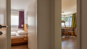 A bedroom with a wooden bed, a small bedside table, and a window with curtains. - Fourteen 2 1 Zell am See S P (Zell am See)
