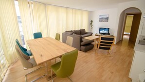 A modern living room with a wooden dining table, green and blue chairs, a grey sofa, and a TV on a wooden stand. - Apartment Zell City - Next to ski Lift and Town (Zell am See)