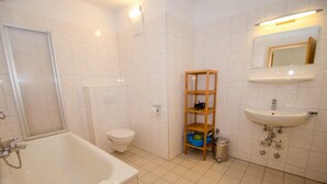 A bathroom with a bathtub, toilet, shelf with toiletries, and a sink. - Apartment Zell City - Next to ski Lift and Town (Zell am See)