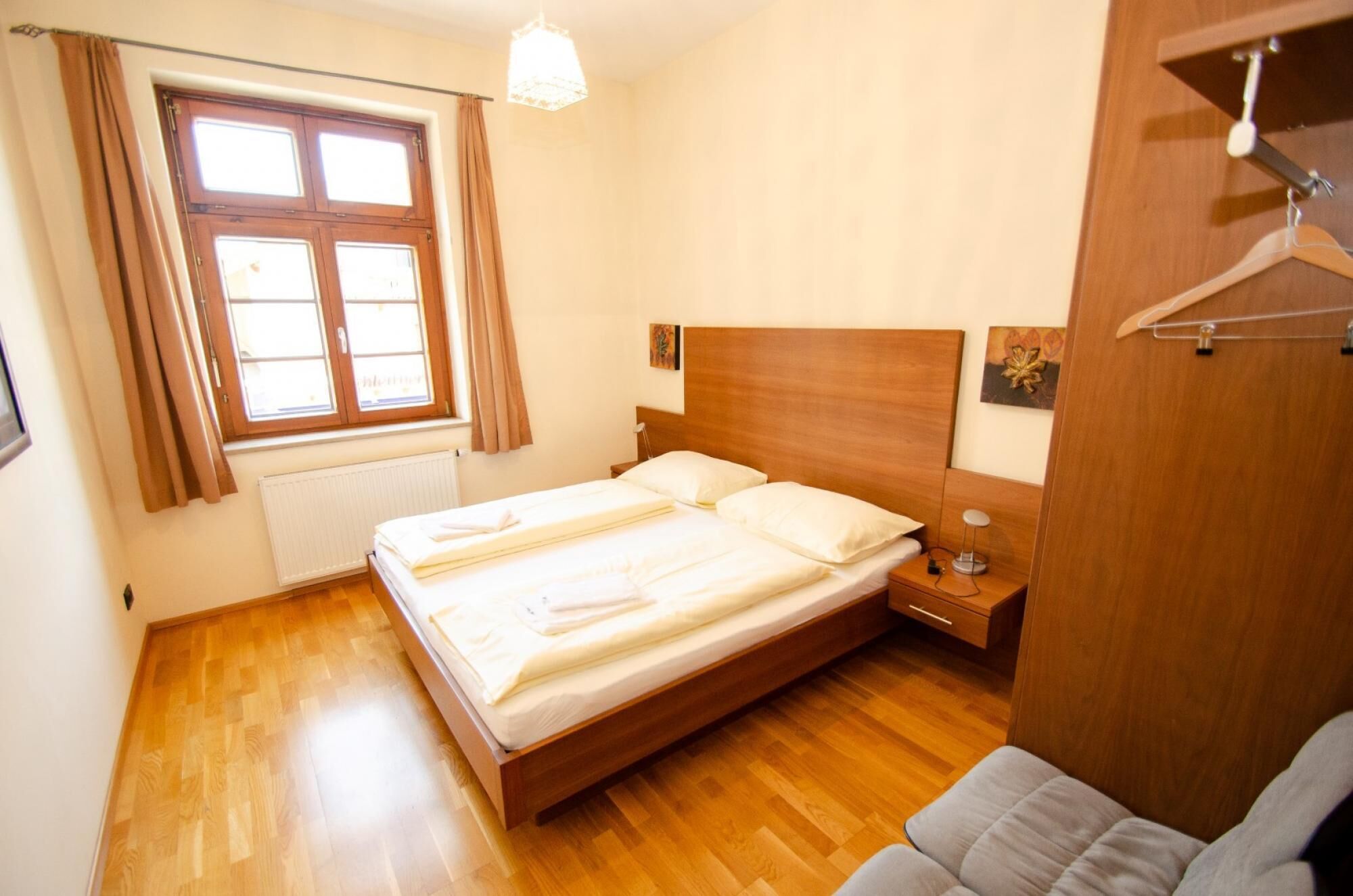 Um quarto bem arrumado com uma cama de casal, uma mesa de cabeceira com abajur, um guarda-roupa de madeira e uma janela com cortinas.